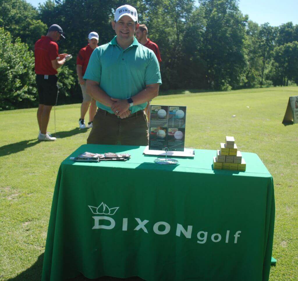 A representative from Dixon Golf stands smiling at their table on the green