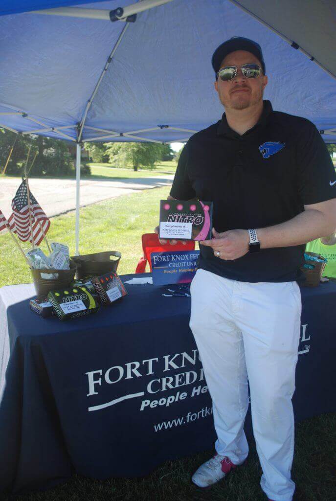 A representative with Ft. Knox Credit Union poses by their table on the green