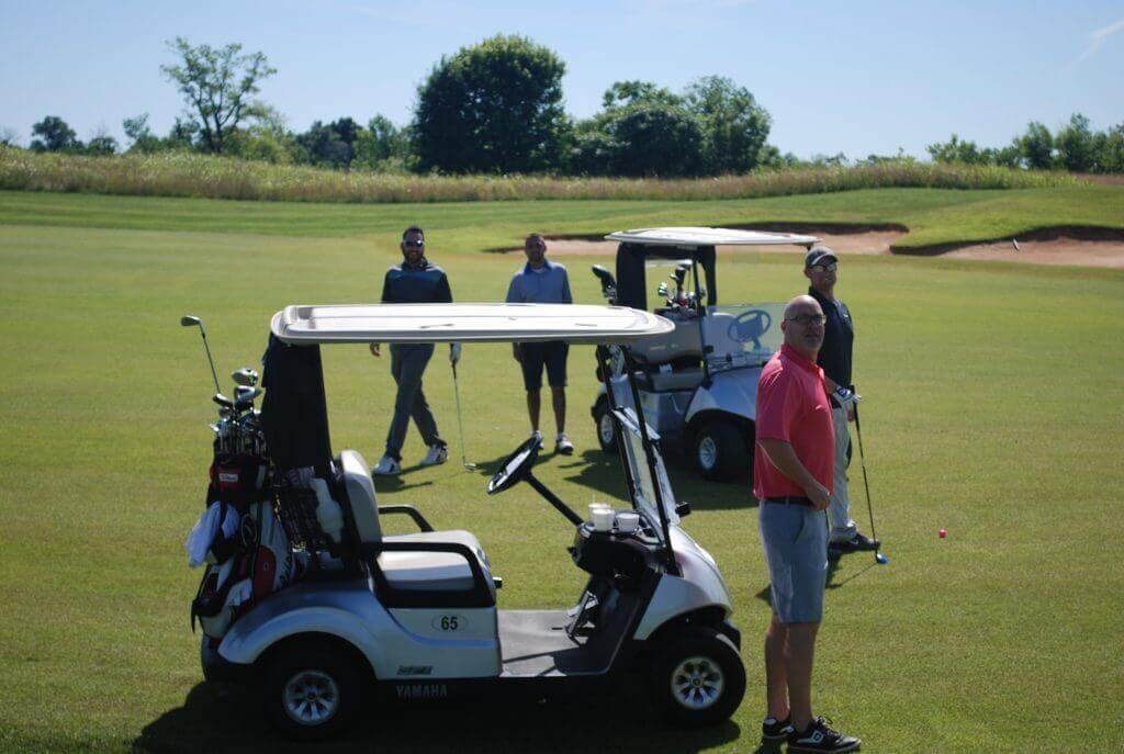 A golf team stands by their carts while in the middle of collecting their golf balls from the green