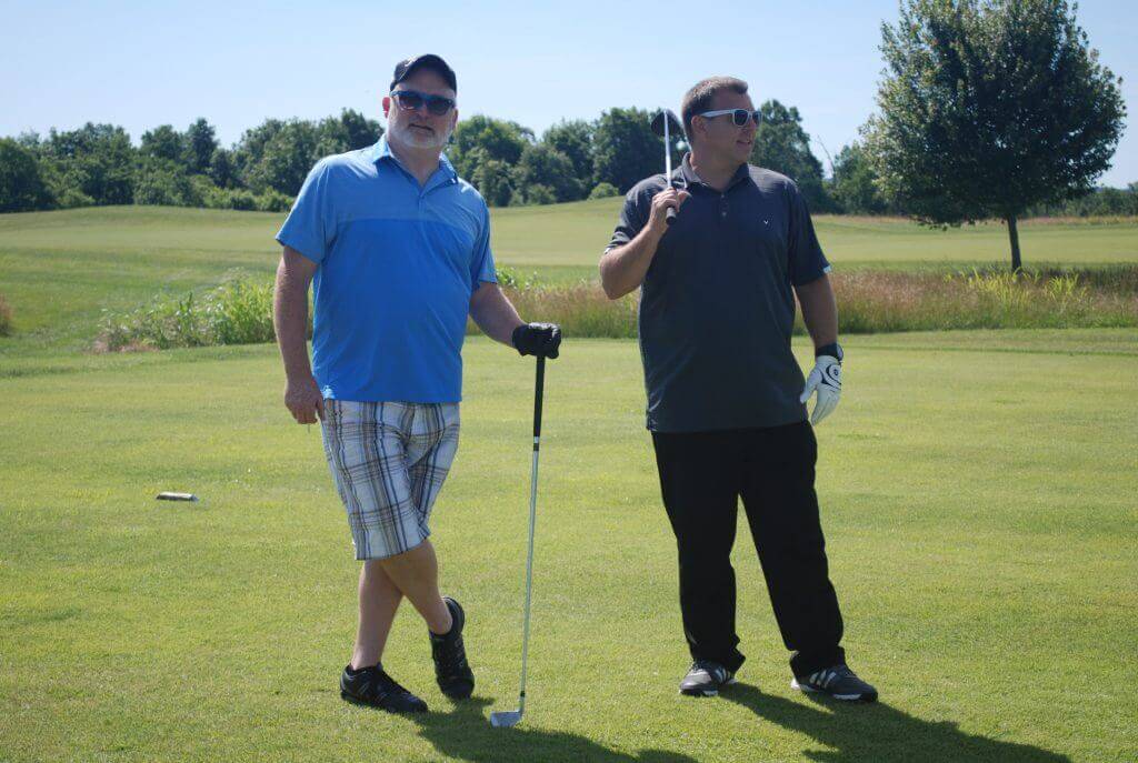Two golfers pose while holding their clubs on the green